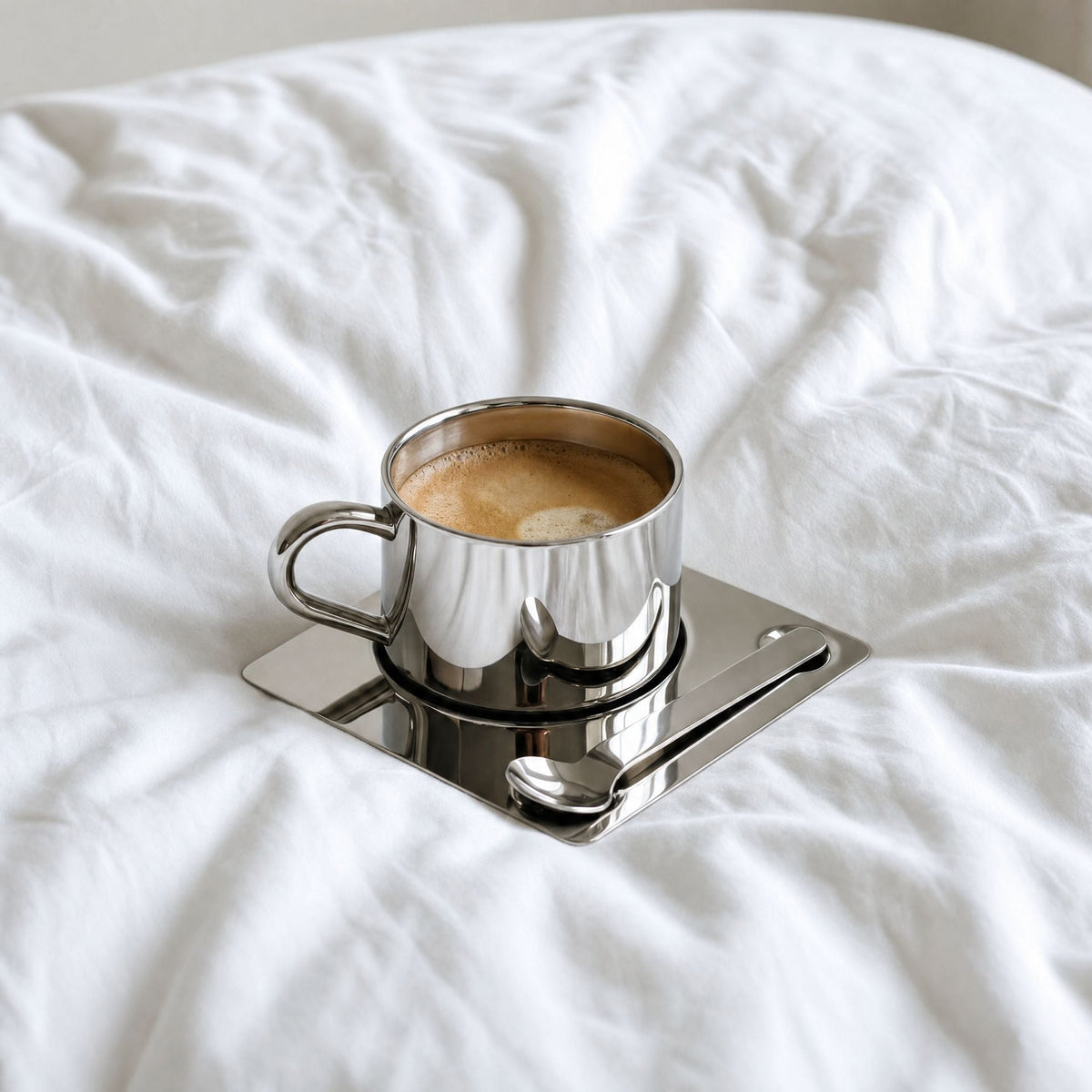 Silberfarbene Tasse mit Untertasse und Löffel in spiegelnder Optik