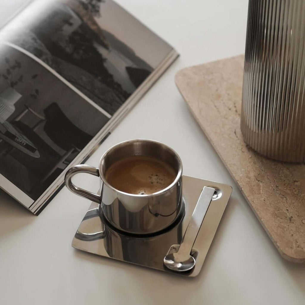 Silberfarbene Tasse mit Untertasse und Löffel in spiegelnder Optik