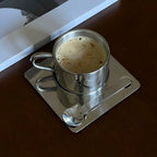 Silberfarbene Tasse mit Untertasse und Löffel in spiegelnder Optik
