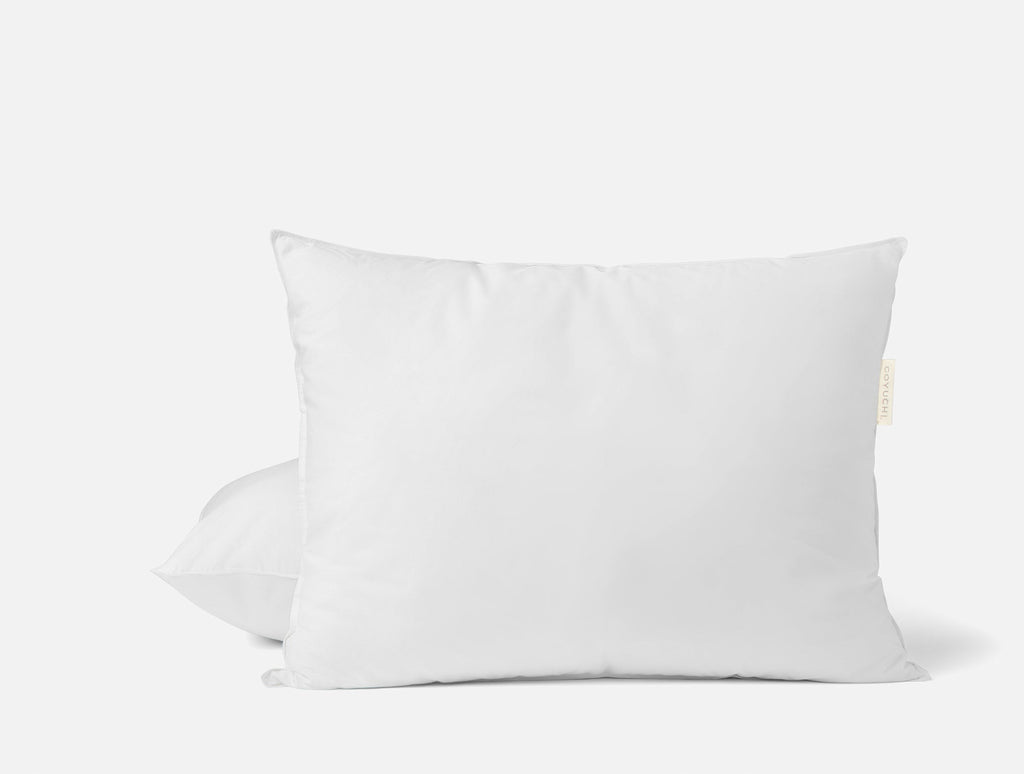 Weißes Kopfkissen mit Daunenfedern auf einem Bett