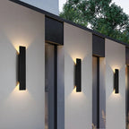 Schwarze vertikale LED-Außenwandleuchte mit warmweißem Licht an einer Fassade